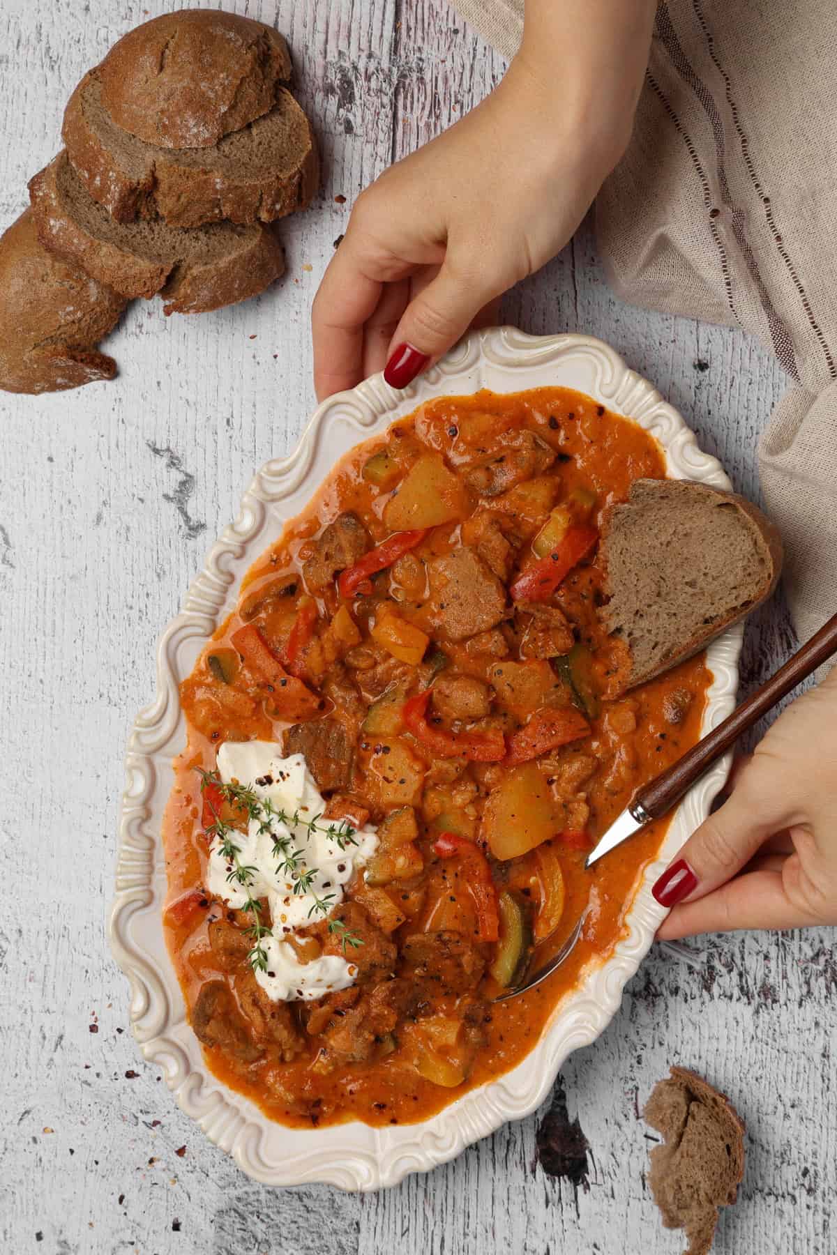 Two hands holding a white serving platter filled with gyro stew.