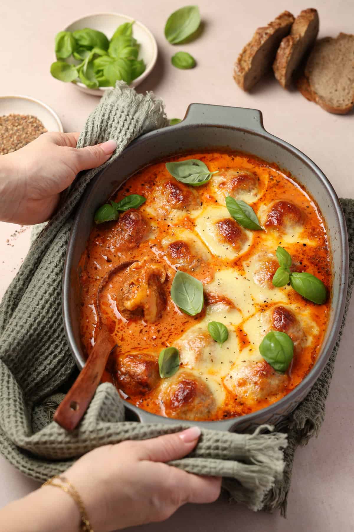 Two hands holding a baking dish filled with Tuscan meatballs.