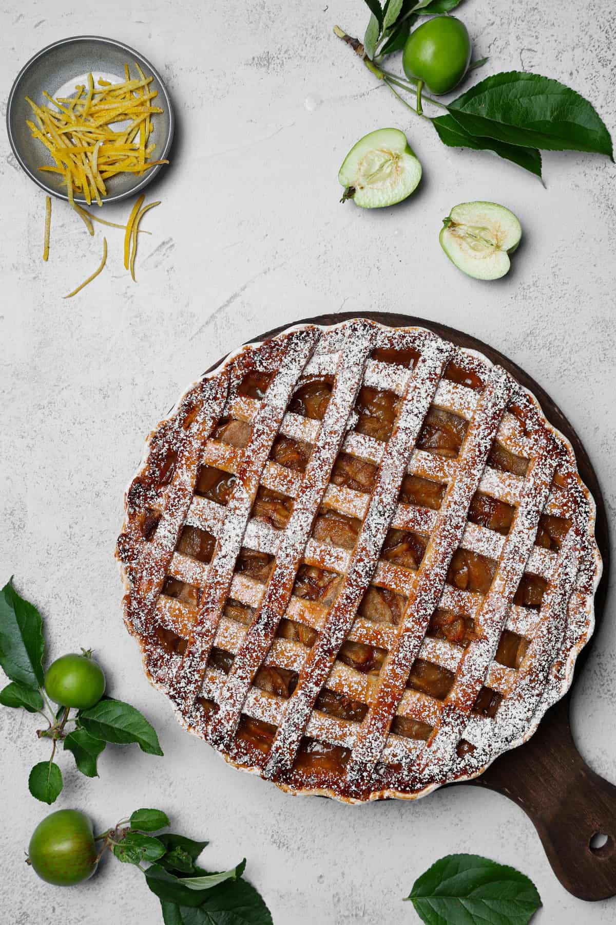 An apple pie served on a round wooden tray with cozy decorations.