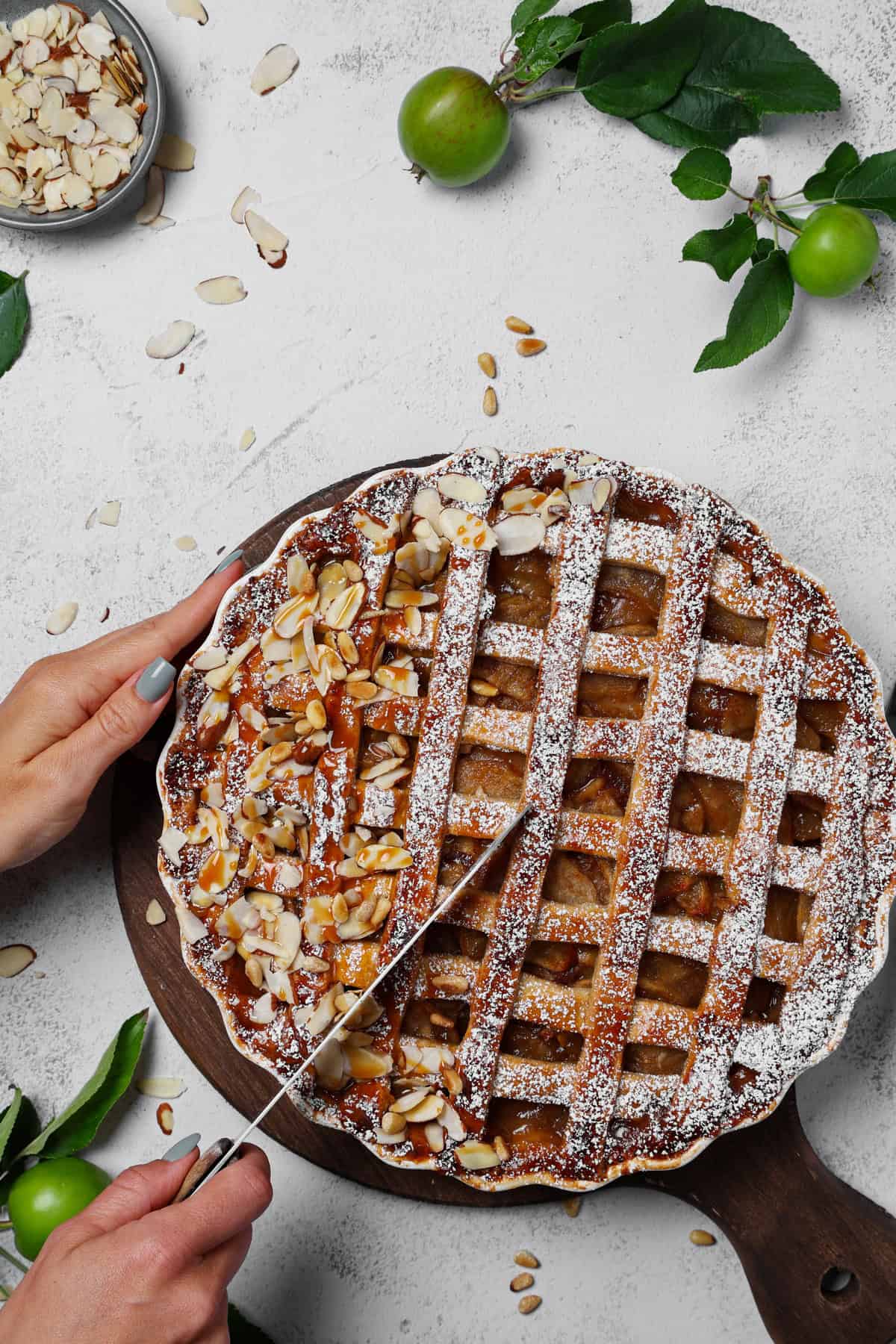 Two hands slicing an apple pie on a wooden tray.
