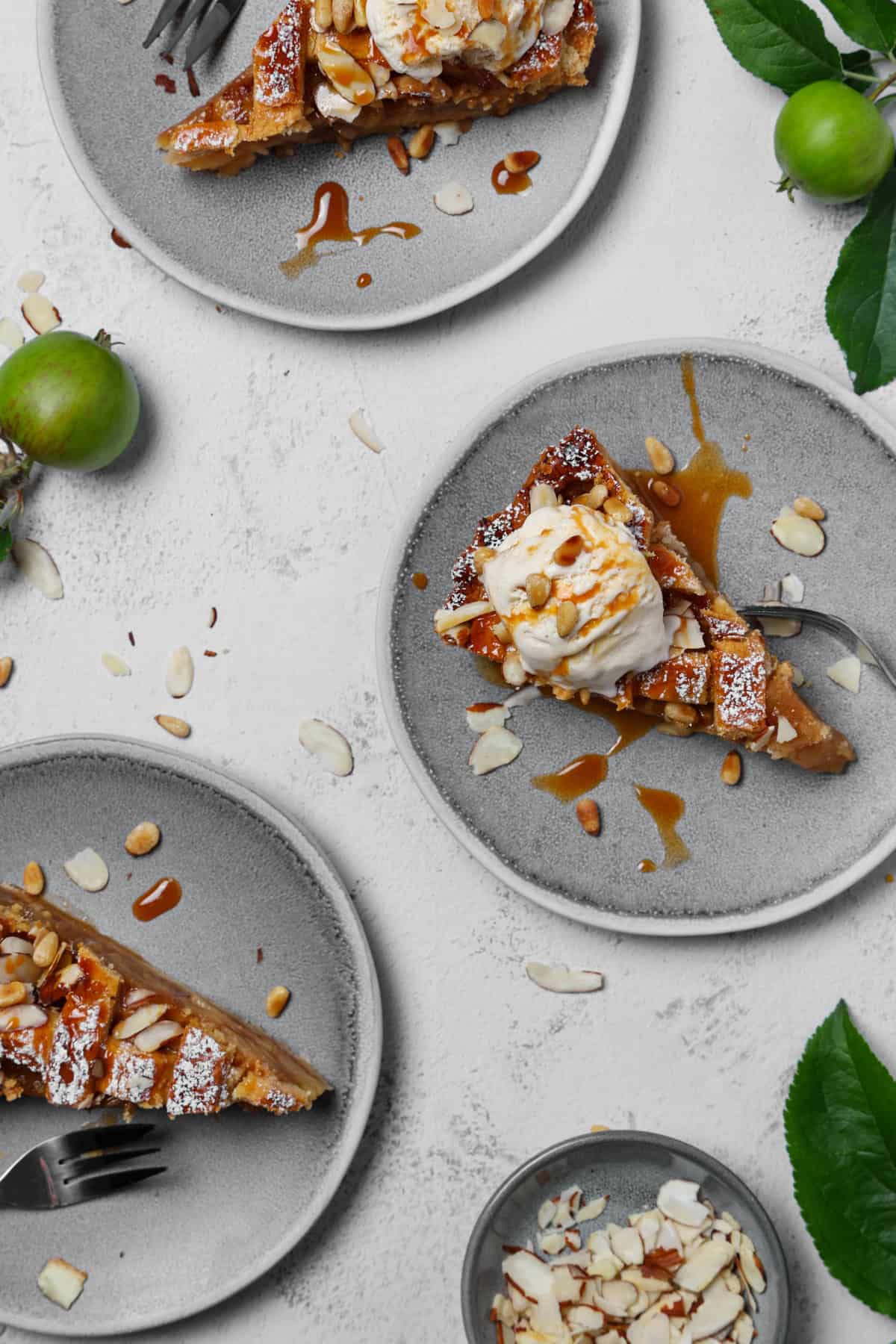 Three slices of apple pie on plates, served with a scoop of vanilla ice cream.