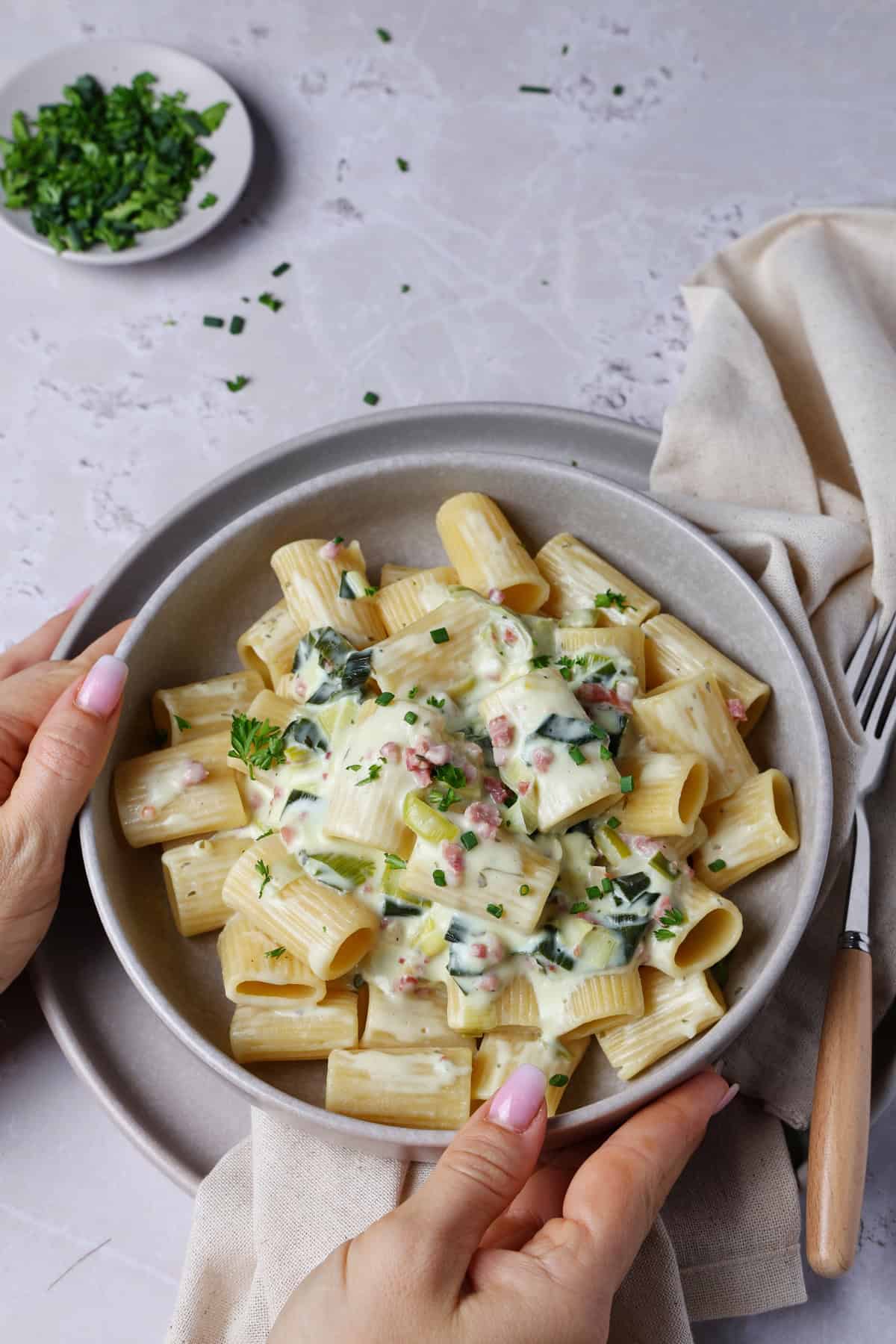 Two hands holding a shallow bowl of cheesy leek pasta.