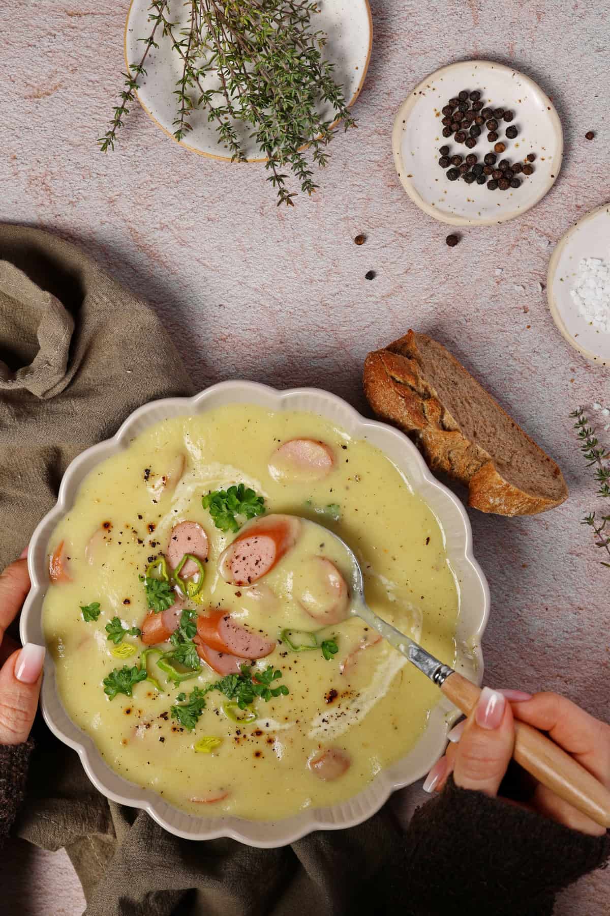 A white soup bowl filled with creamy potato parsnip soup topped with sliced sausages.
