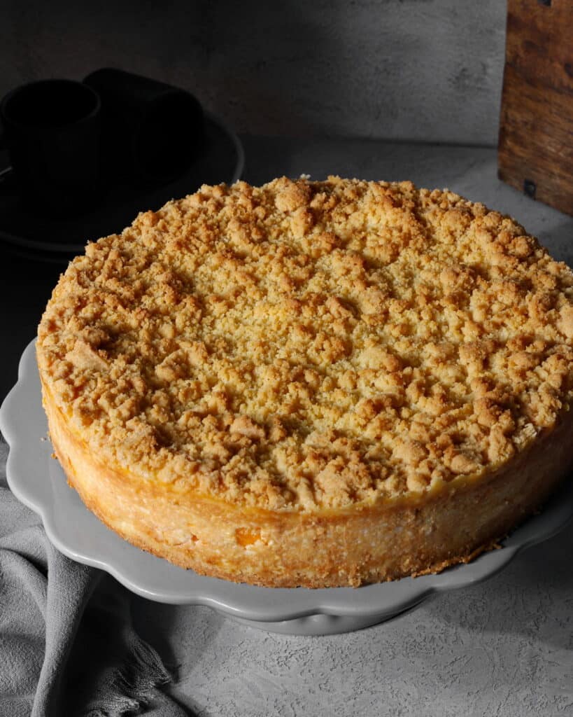 Ein Mandarinen-Schmand-Streuselkuchen auf einem runden Serviertablett.