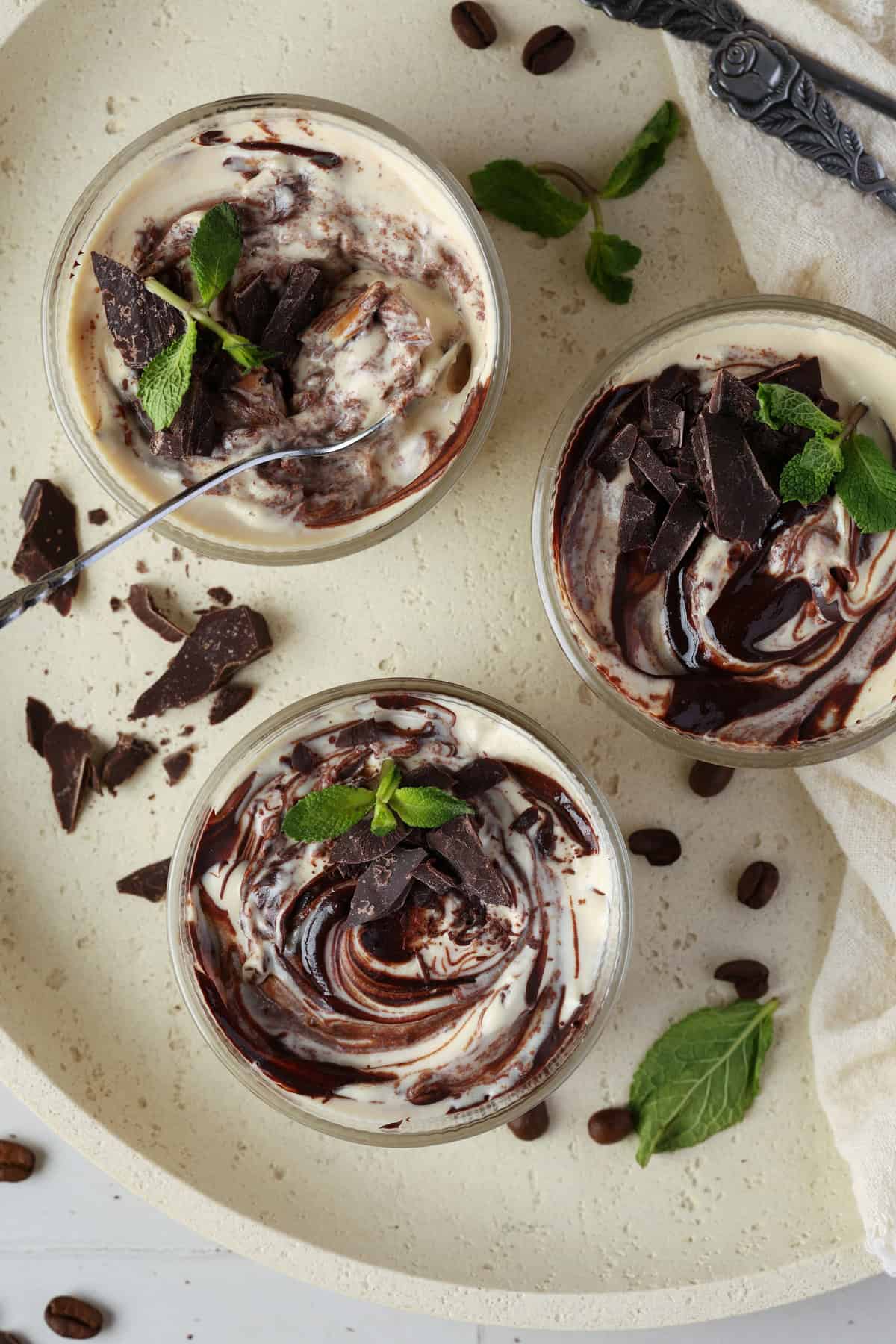 Top-down view of three small glasses with mocha mousse on a light-colored round serving tray.