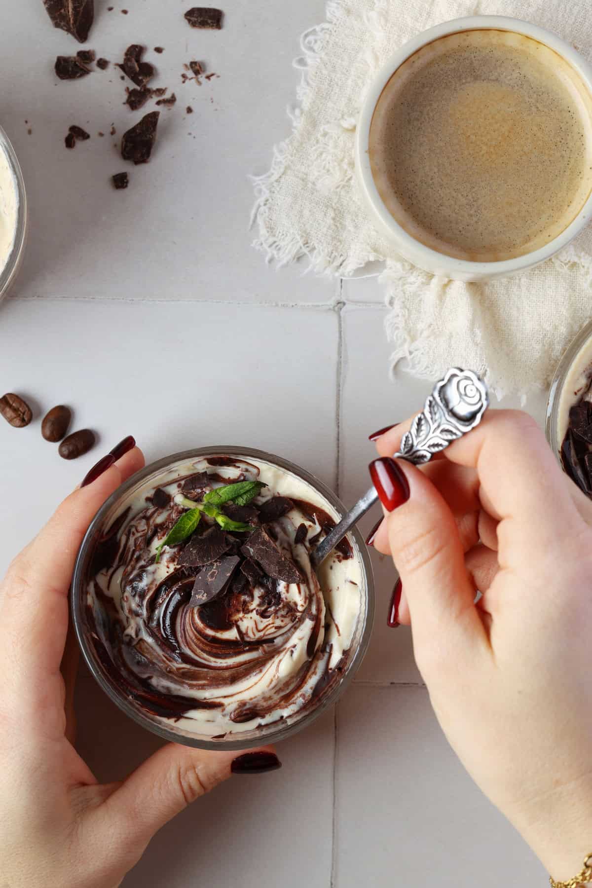 Two hands taking a spoonful of mocha mousse from a small glass bowl.