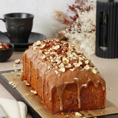 Ein saftiger Nusskuchen mit herablaufendem Schokoguss und grob gehackten Haselnüssen als Topping.