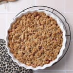 Ein Pfirsich-Crumble mit Haselnussstreuseln in einer runden, weißen Auflaufform.