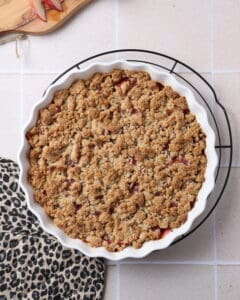 Ein Pfirsich-Crumble mit Haselnussstreuseln in einer runden, weißen Auflaufform.