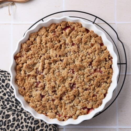 Ein Pfirsich-Crumble mit Haselnussstreuseln in einer runden, weißen Auflaufform.