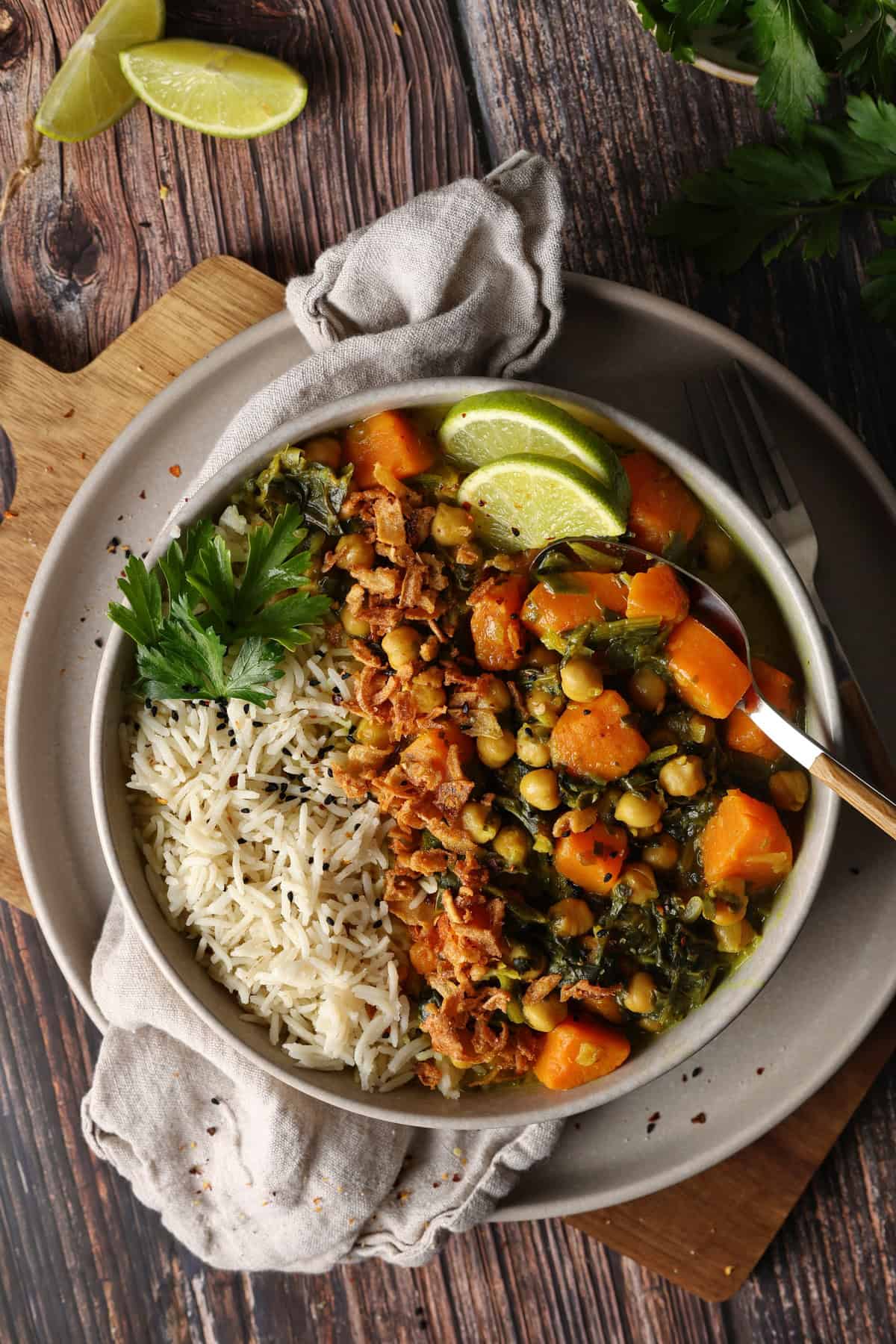 Ein tiefer Teller mit Süßkartoffel-Curry mit Spinat und Kichererbsen, Reis und Zitronenspalten.