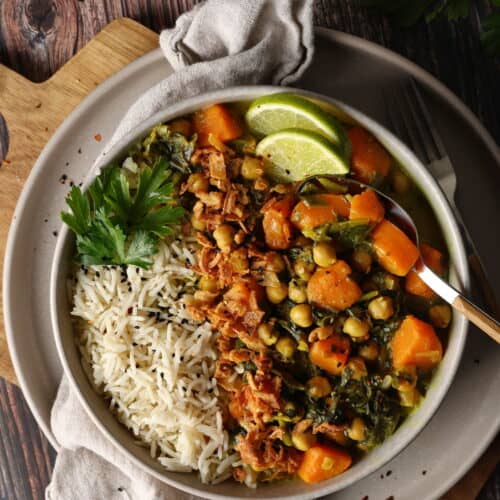 Ein Teller mit Süßkartoffel-Curry mit Spinat und Kichererbsen, Reis und Zitronenspalten.