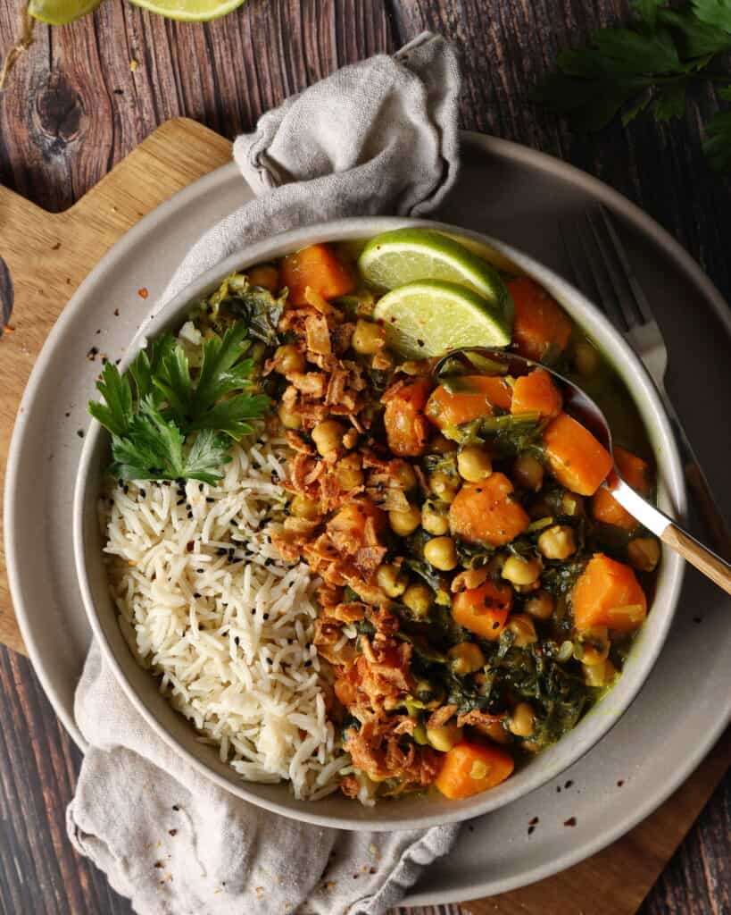 Ein Teller mit Süßkartoffel-Curry mit Spinat und Kichererbsen, Reis und Zitronenspalten.