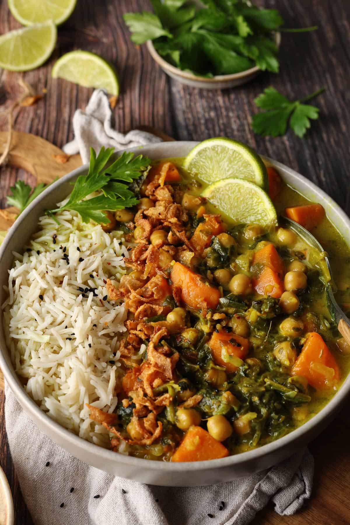 Close-up of a plate of sweet potato curry with spinach and chickpeas, served with rice and lemon wedges.