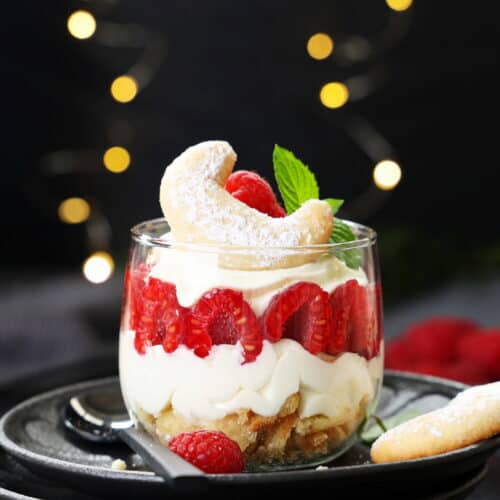 Geschichtetes Vanillekipferl-Himbeer-Dessert im Glas mit Mascarpone-Creme, frischen Himbeeren und einem Kipferl als Deko.