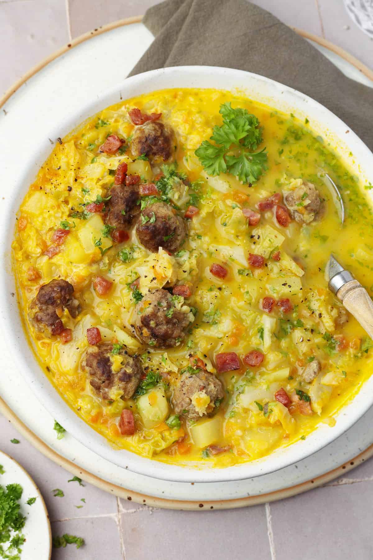 A close-up of a white bowl filled with savoy cabbage soup and meatballs.