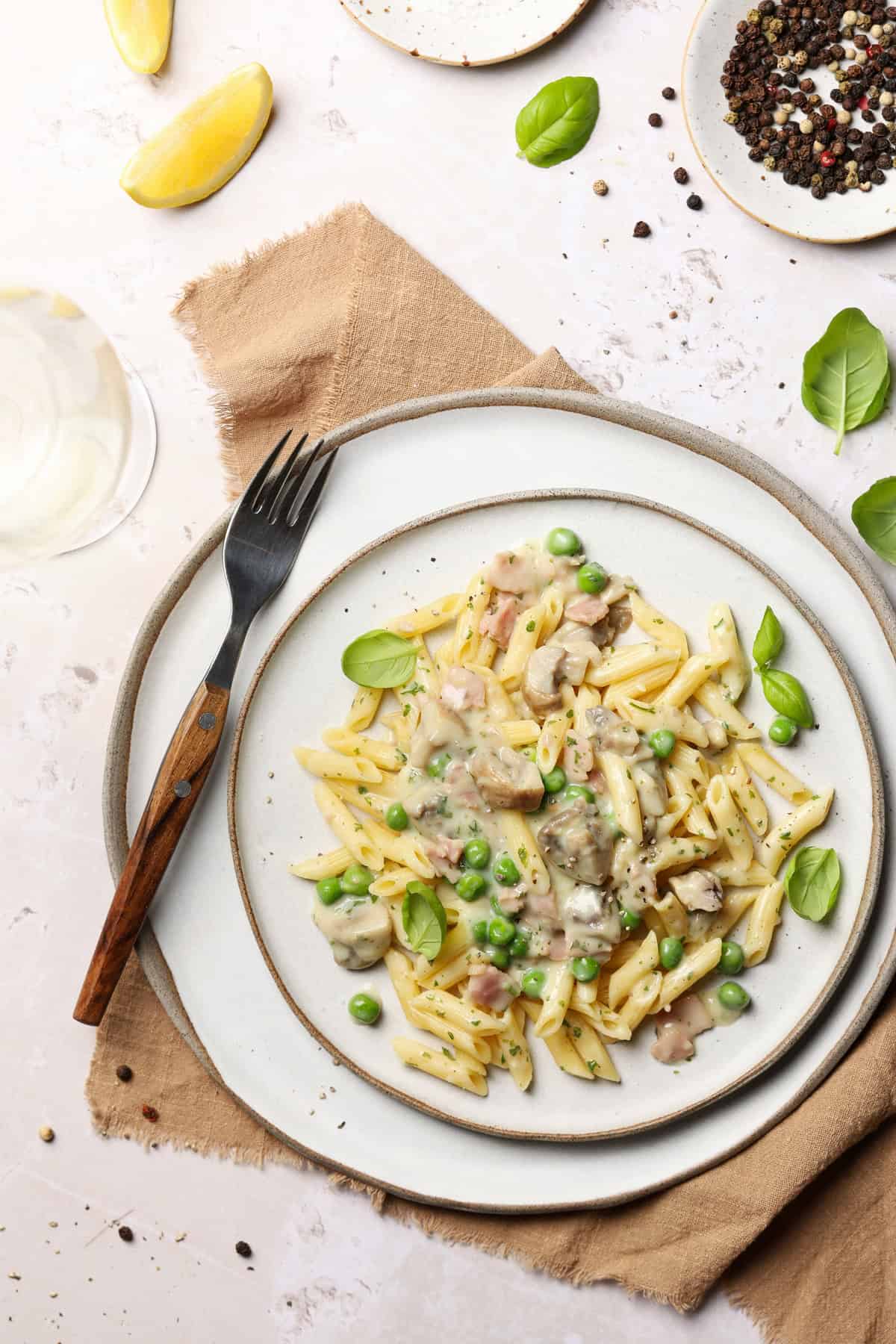 Ein Teller mit Zitronen-Rahm-Pasta mit Champignons & Erbsen. Als Deko Basilikumblätter.