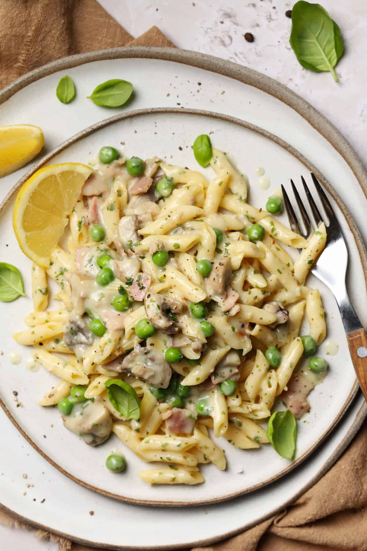 A close-up of a plate of creamy lemon pasta with mushrooms, peas, and a lemon wedge.