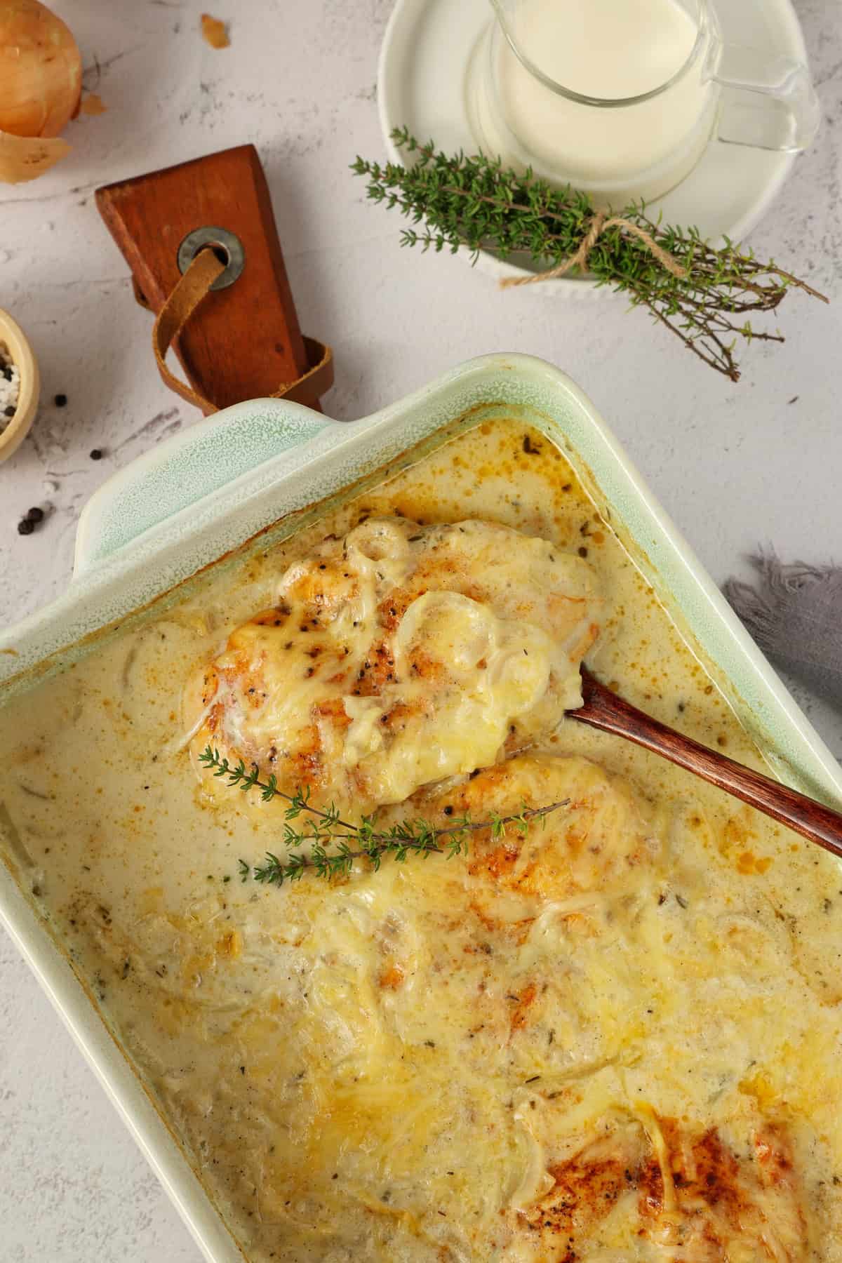 A white baking dish filled with creamy onion chicken topped with fresh garnishes.