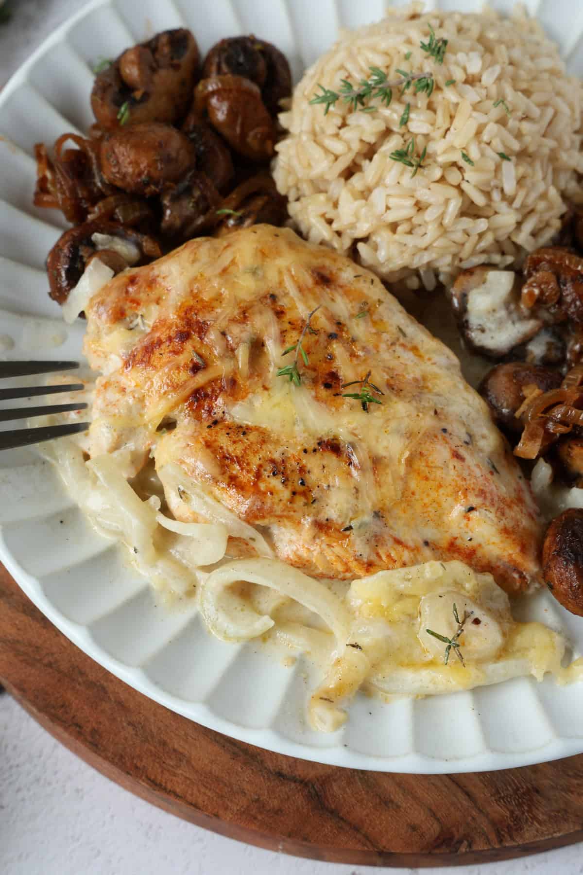 A close-up of creamy French onion chicken served with mushrooms and rice on a white plate.