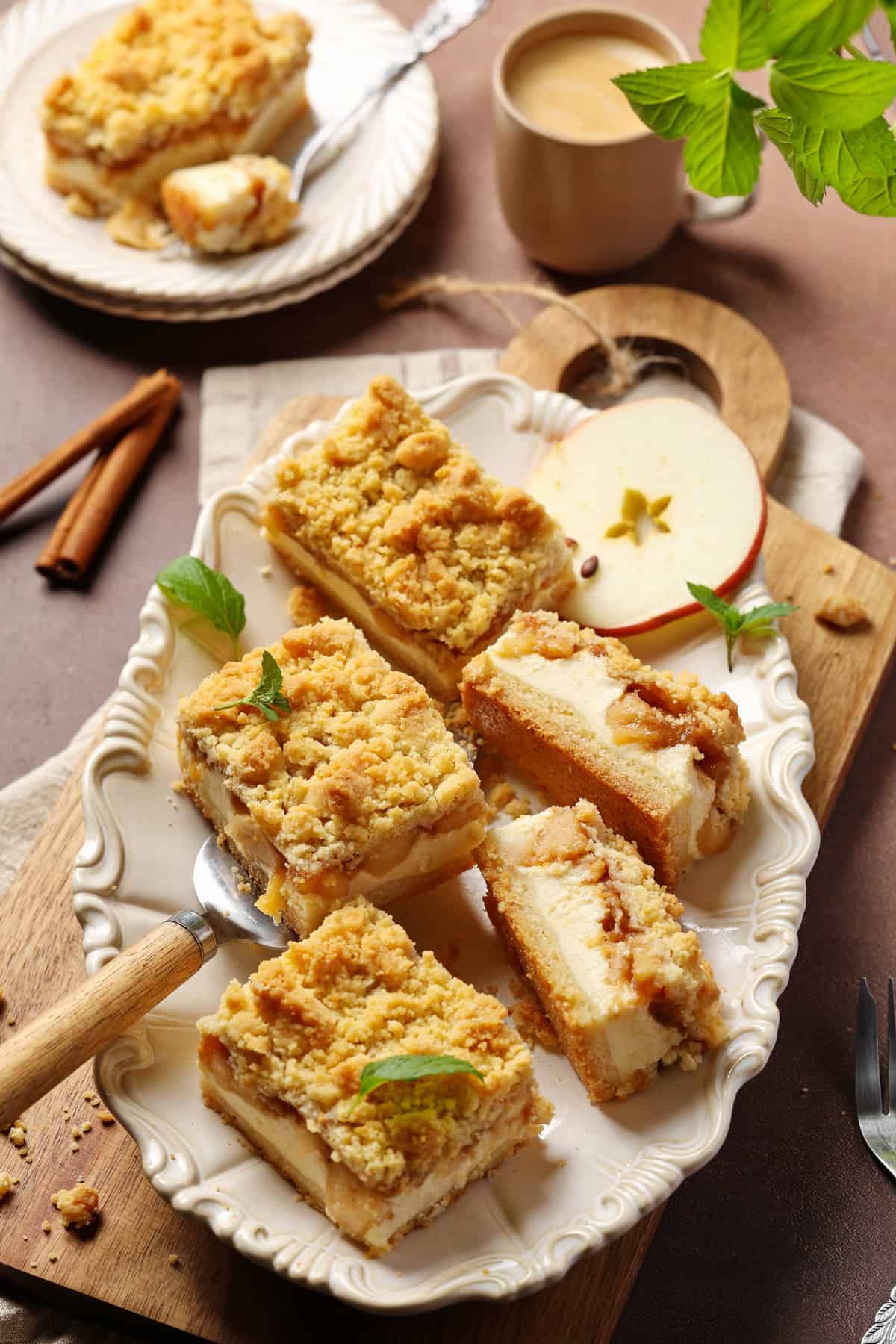 Several slices of apple streusel cheesecake on an oval white serving platter, garnished with an apple slice.