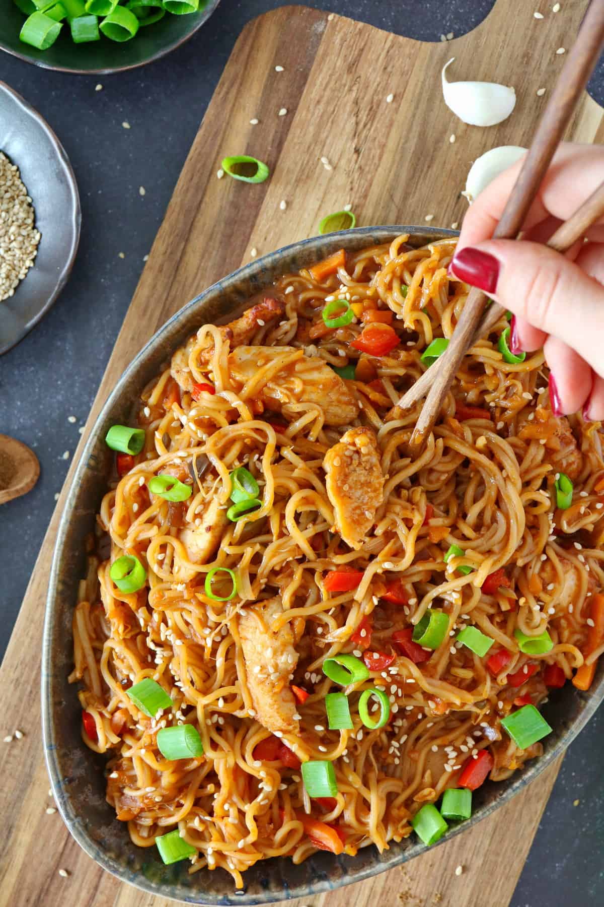 Chopsticks lifting a portion of Asian chicken noodles out of an oval bowl.