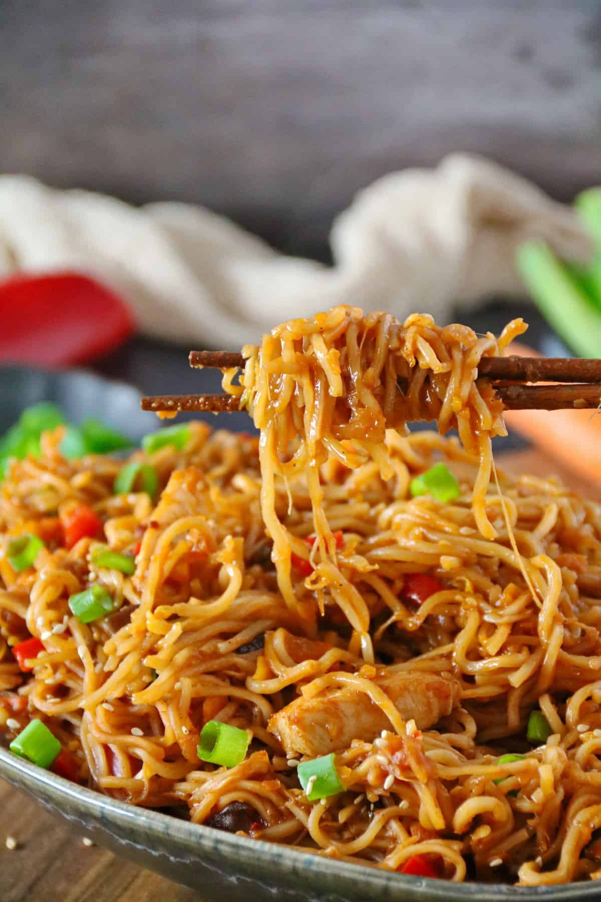 A portion of Asian chicken noodles lifted with chopsticks over a serving bowl.
