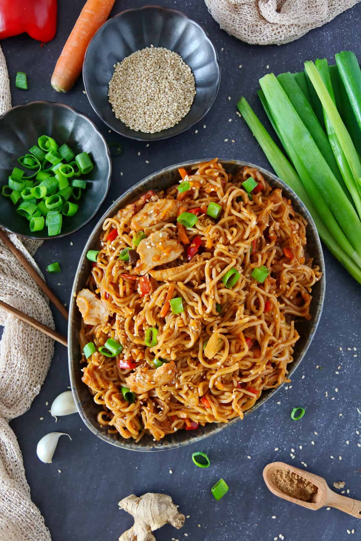An oval bowl filled with Asian chicken noodles surrounded by garnish.