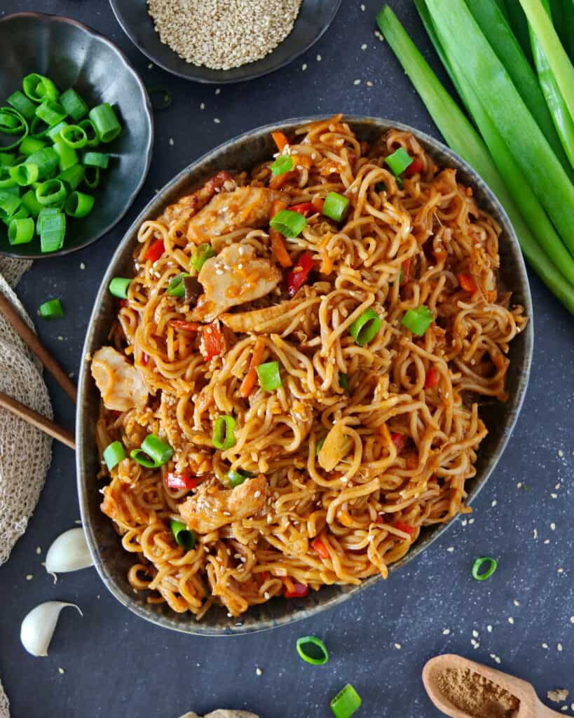 An oval bowl with Asian noodles and chicken.