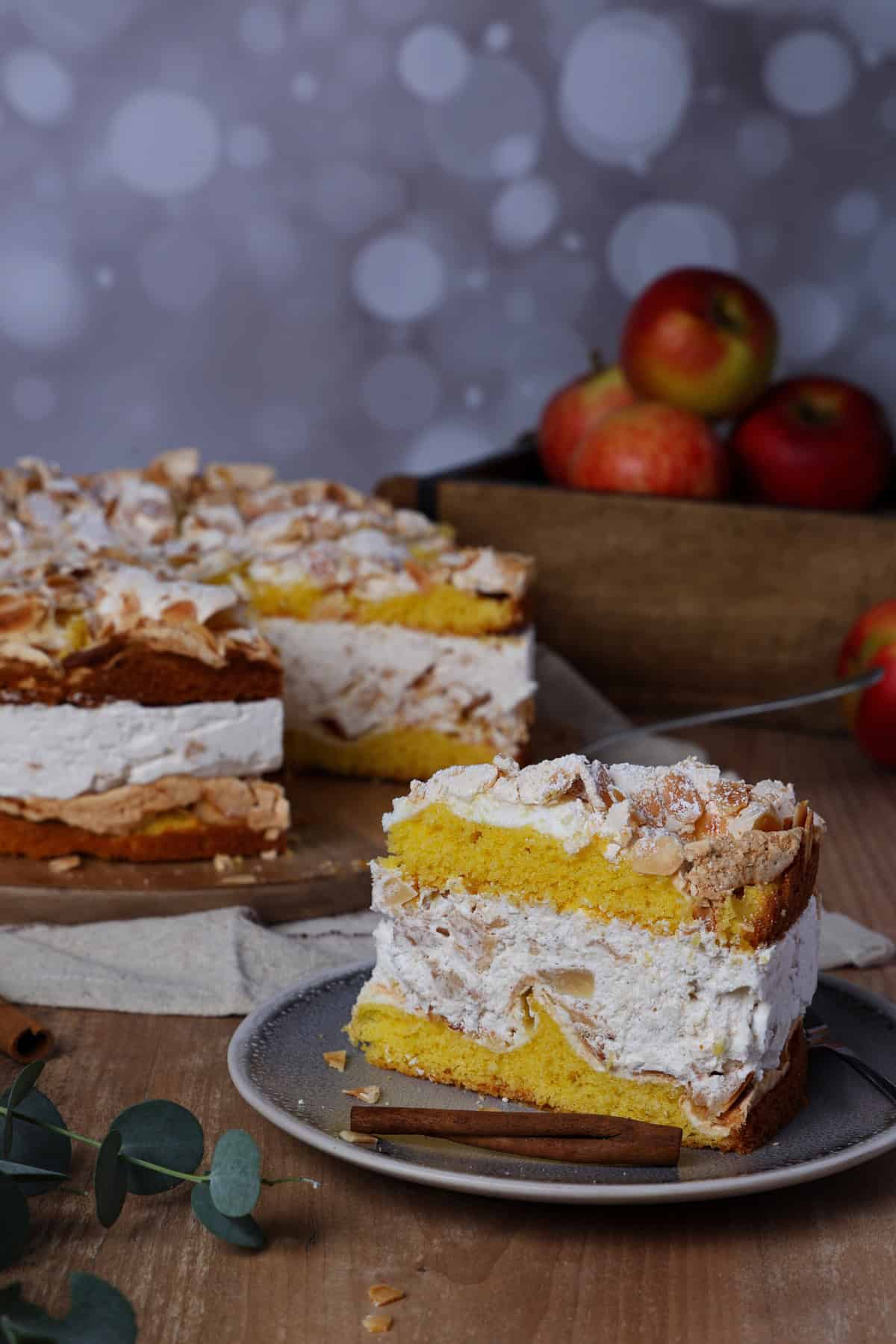 A slice of baked apple meringue cake on a small plate. Behind it is the rest of the baked apple meringue cake.