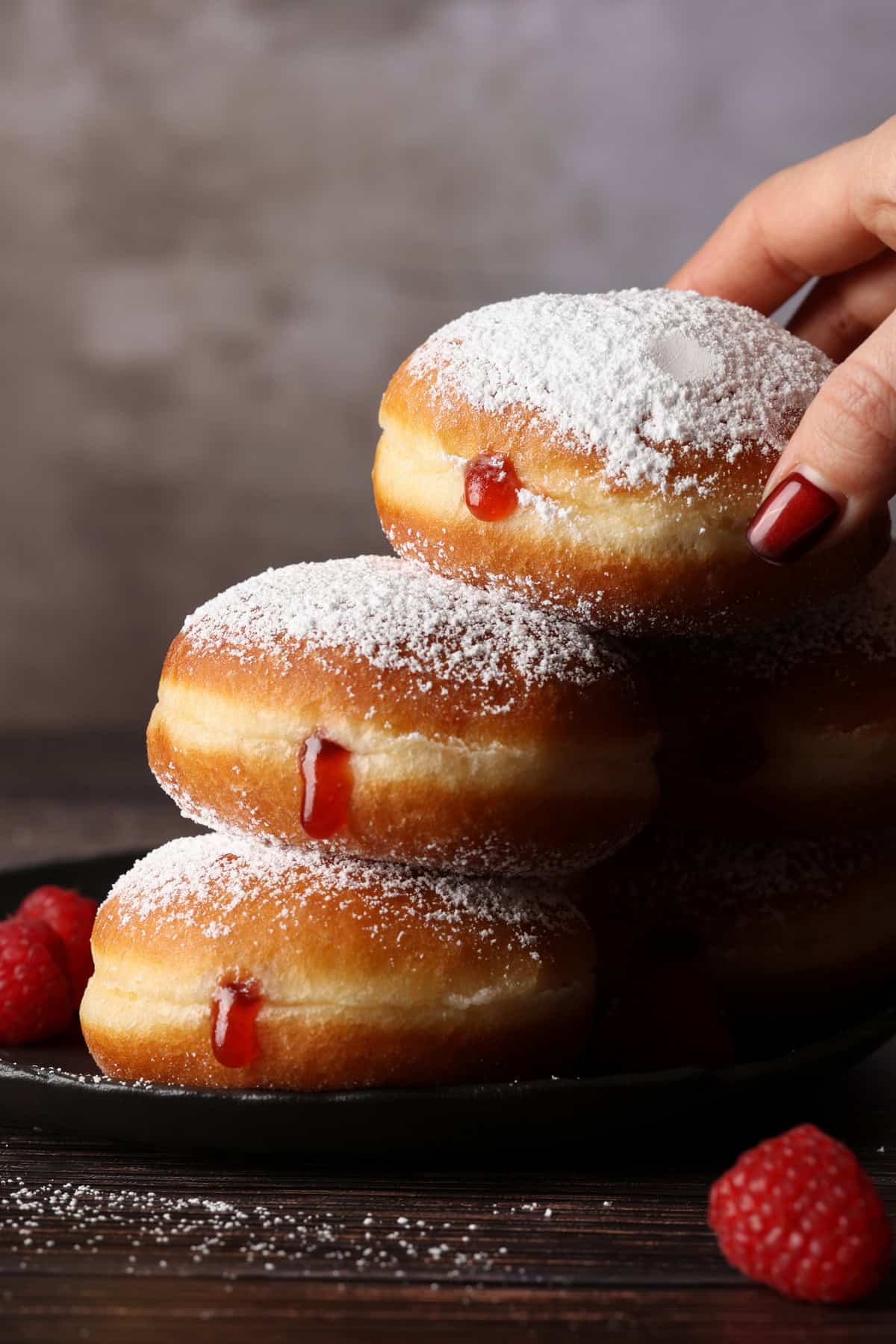 A hand stacking three jelly donuts on top of each other.
