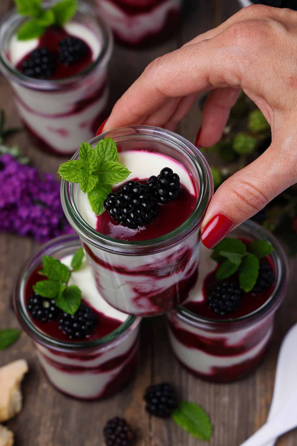 A hand stacking three glasses of blackberry mascarpone trifle on top of each other.