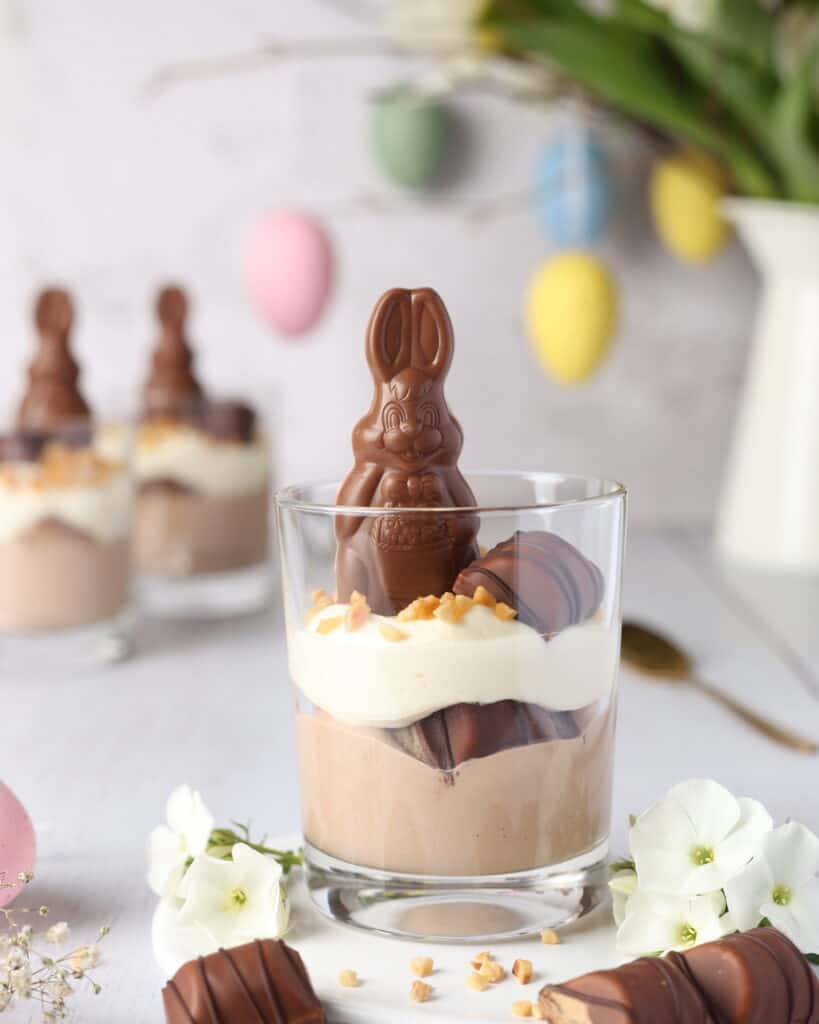 Two-tone layered Bueno dessert in a glass, decorated with a chocolate bunny and hazelnuts for Easter.