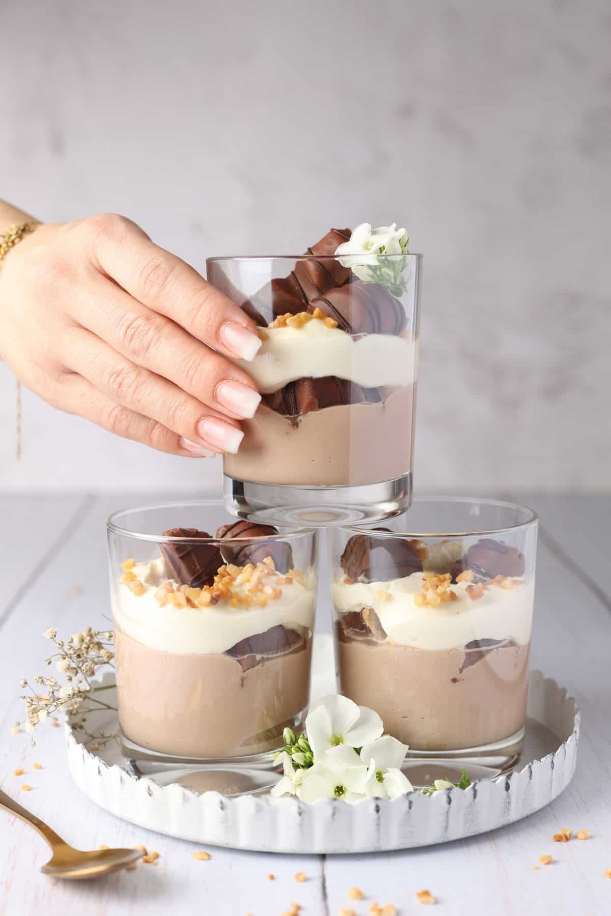 A hand stacking three glasses of Bueno dessert on top of each other.