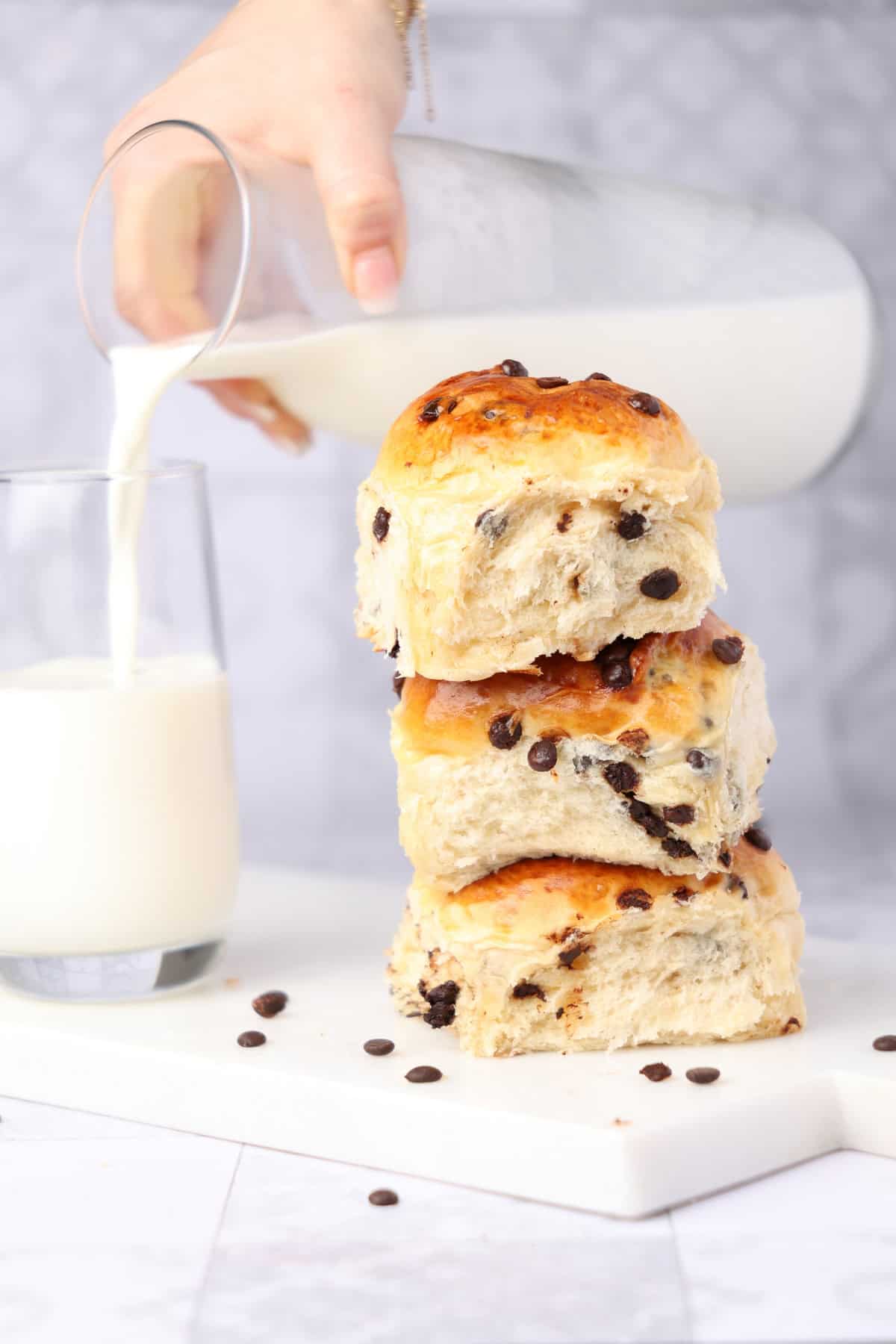 Three stacked chocolate rolls. In the background, a hand is pouring a glass of milk.