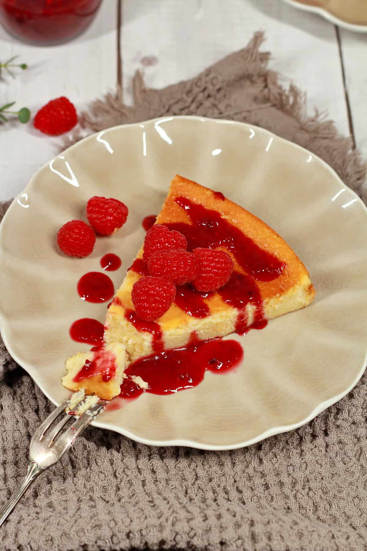 A slice of crustless cheesecake topped with fresh raspberries on a plate.