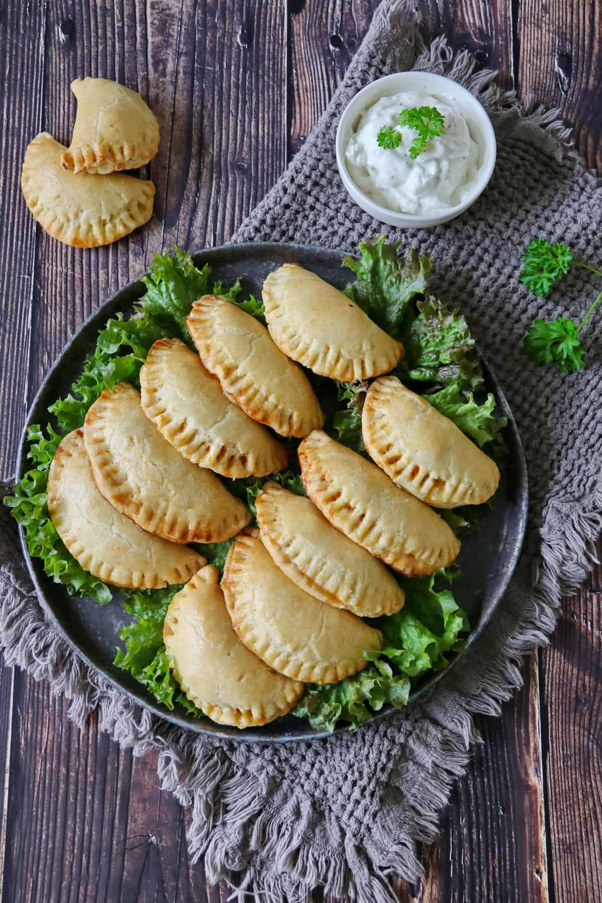 A dark plate filled with beef empanadas next to a small bowl of dipping sauce.