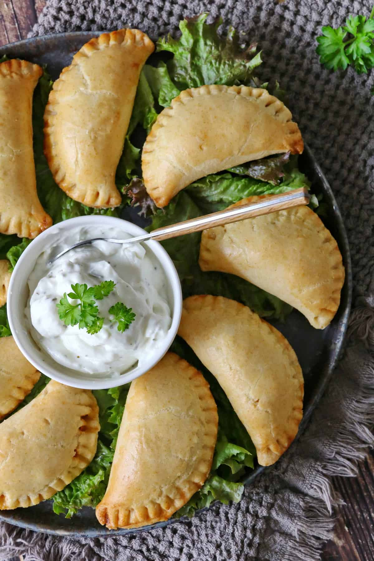 A plate of beef empanadas arranged in a circle, served over salad with a small dipping bowl in the center.