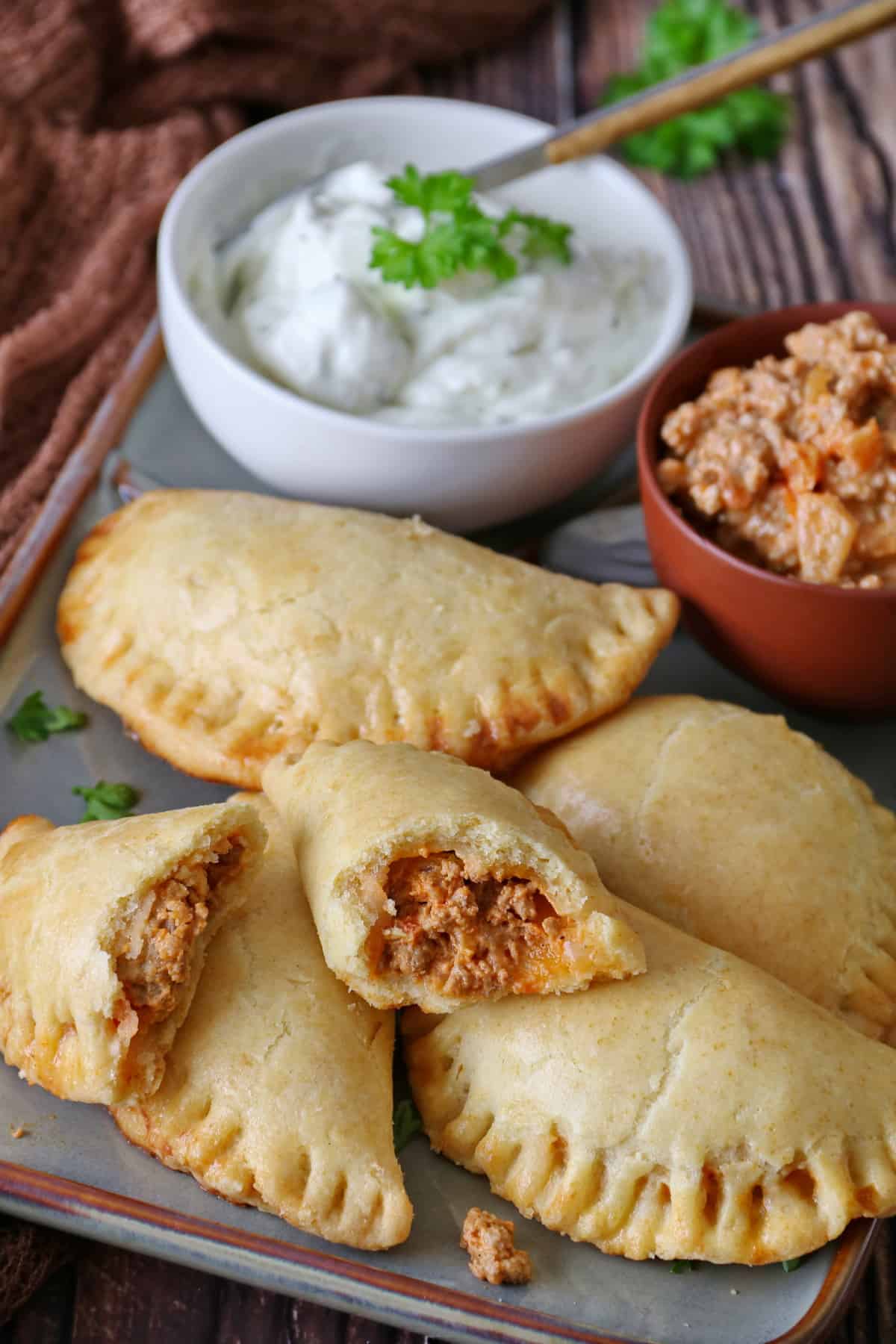 A rectangular serving platter with empanadas, a small bowl of dip, and a small bowl of beef filling.