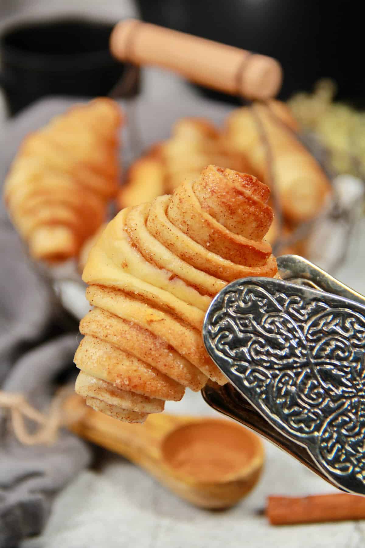 A close-up of a mini Franzbrötchen held with serving tongs.