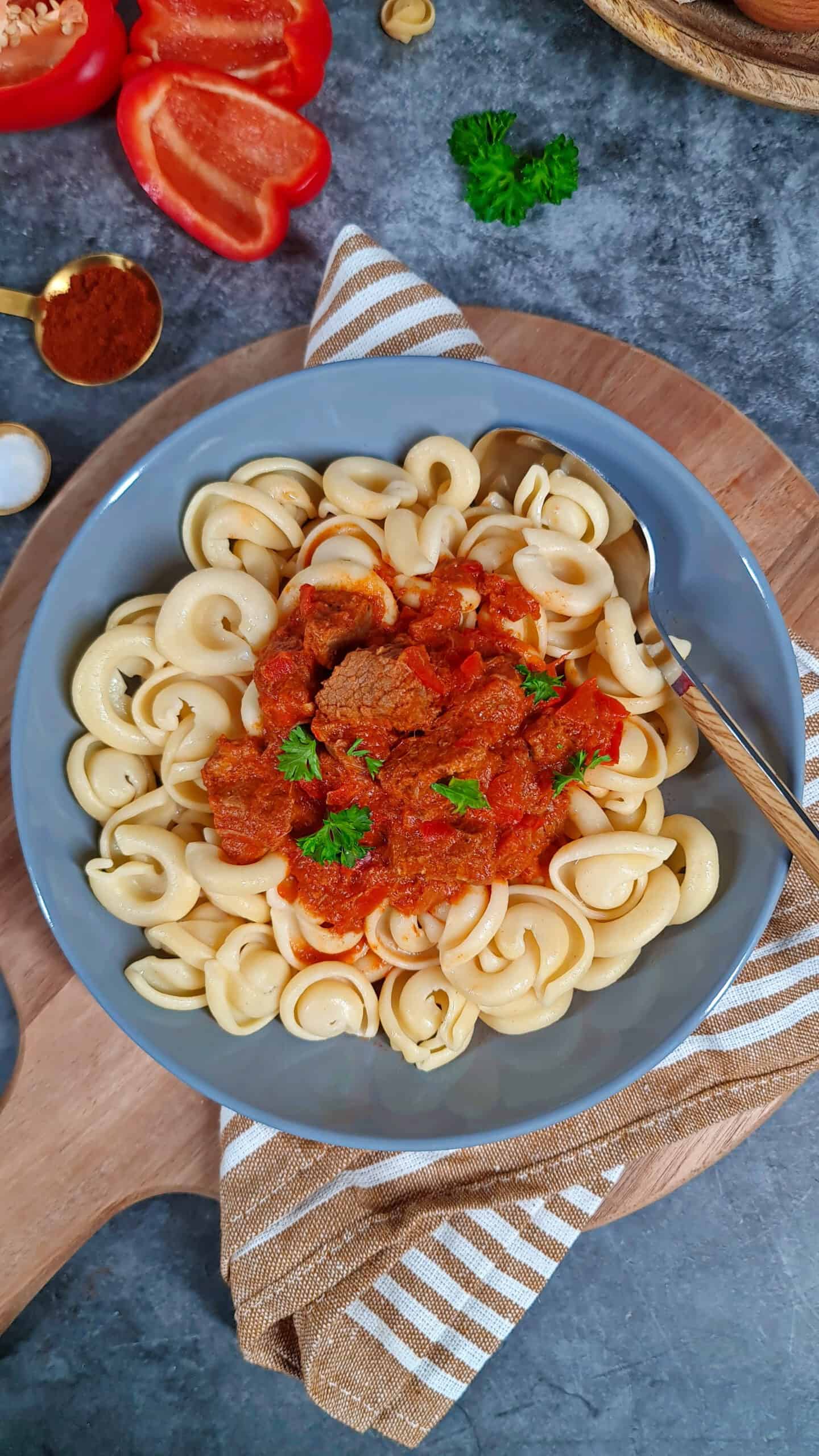 A deep gray bowl filled with beef goulash, bell peppers, and pasta.