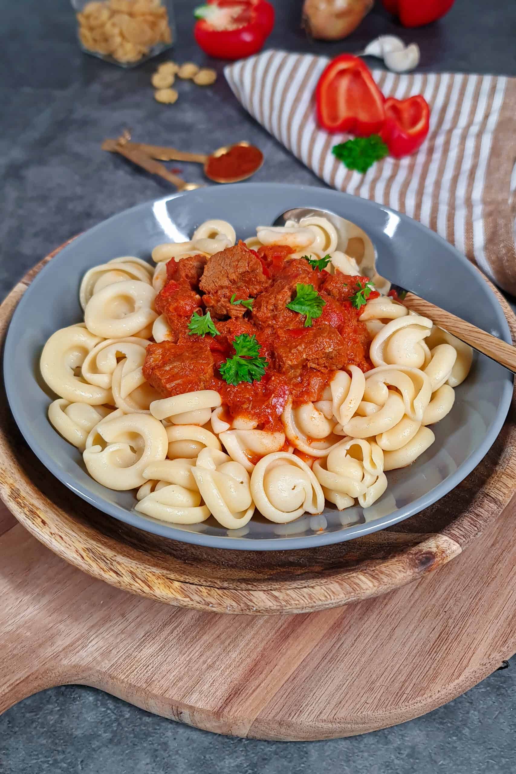 A deep grey bowl filled with beef goulash, bell peppers, and pasta.