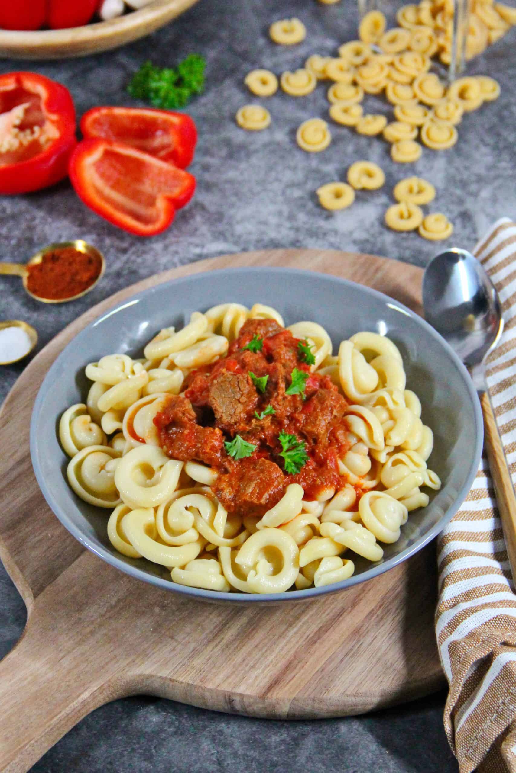 A deep gray bowl filled with beef goulash, bell peppers, and noodles.