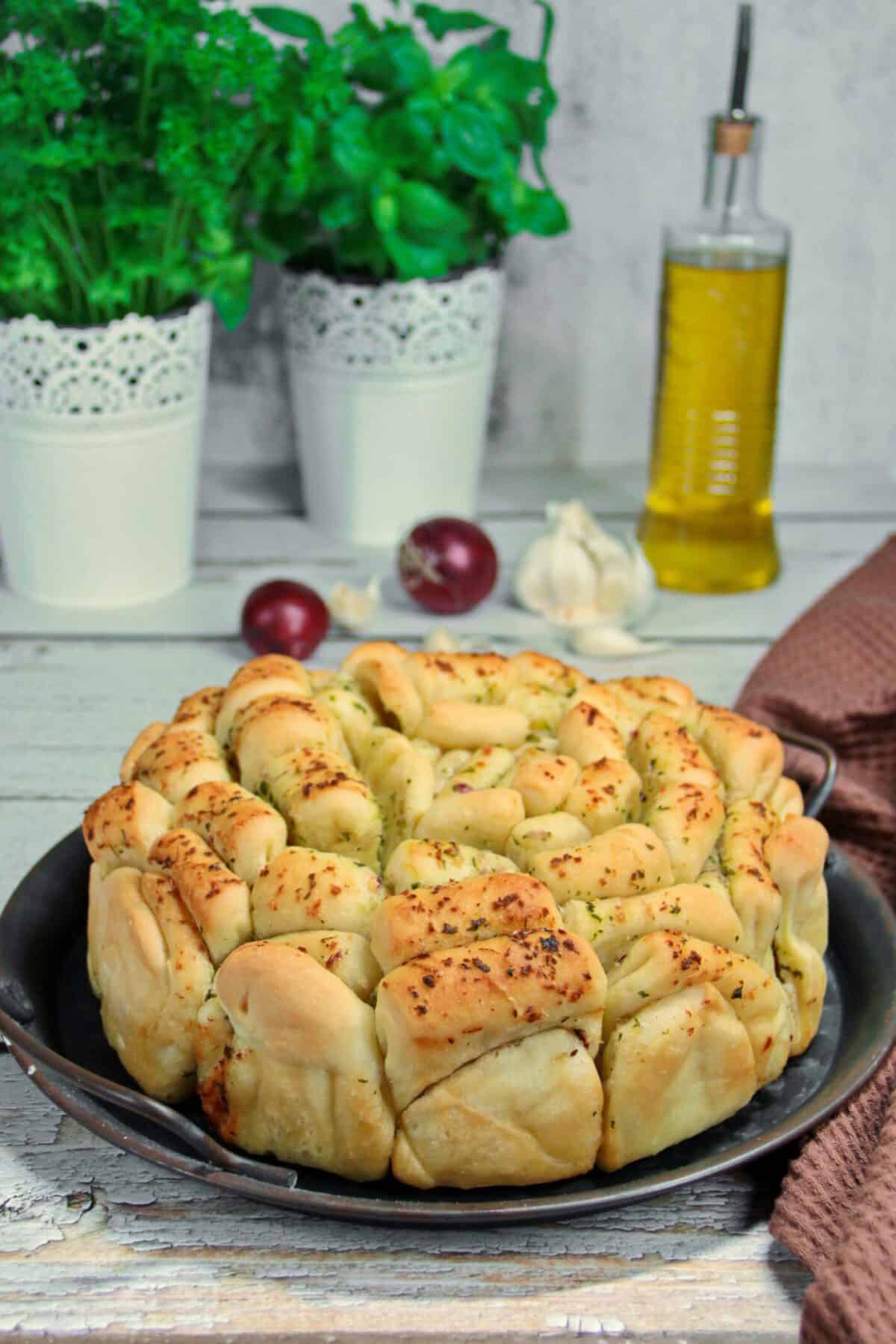 A round herb pull-apart bread served on a metal tray.