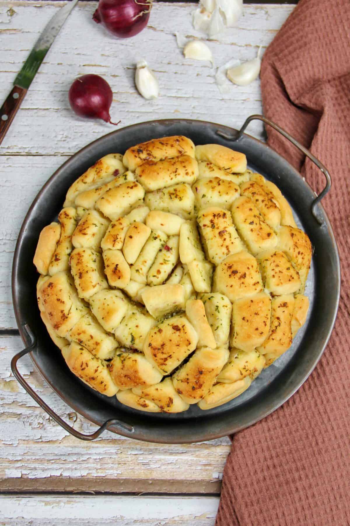 A round herb pull-apart bread served on a metal tray.