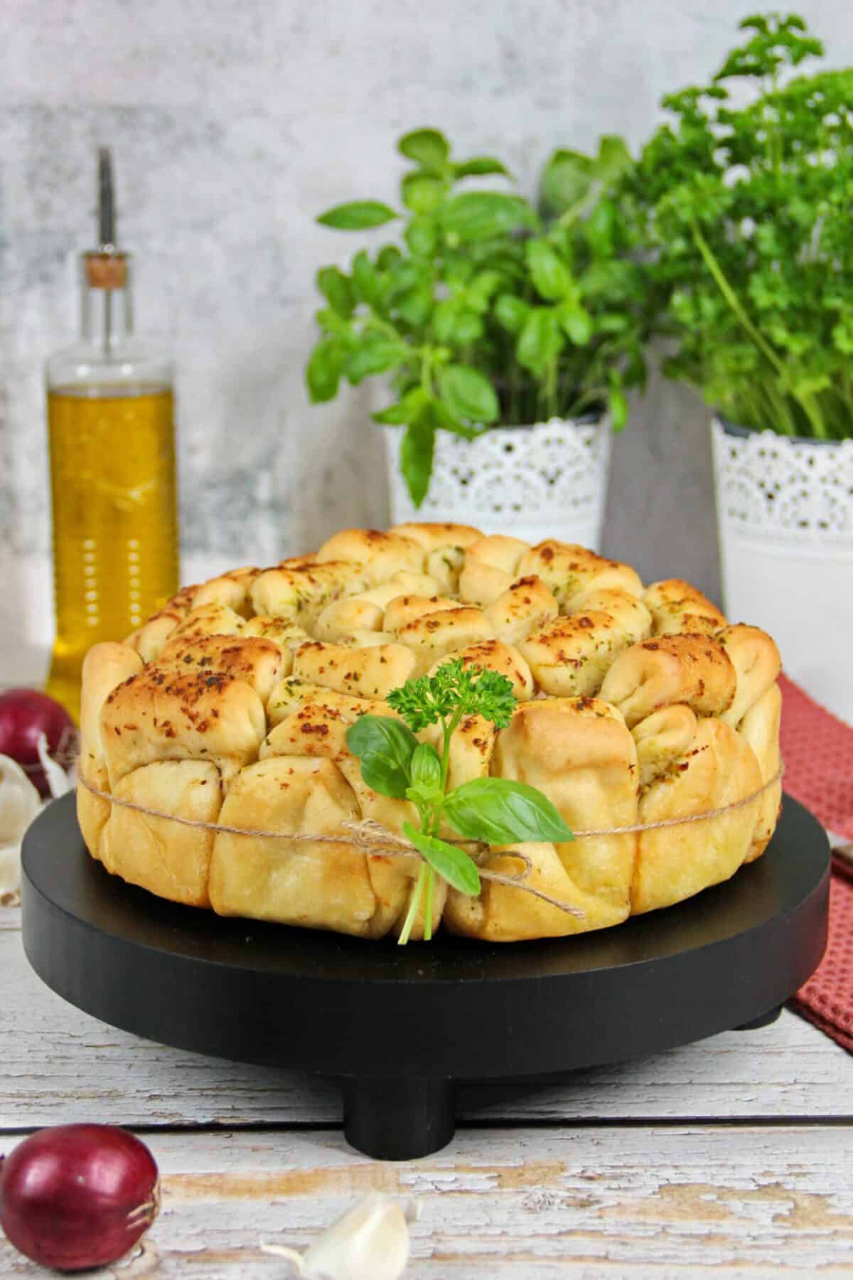 A round herb pull-apart bread on a black serving platter.