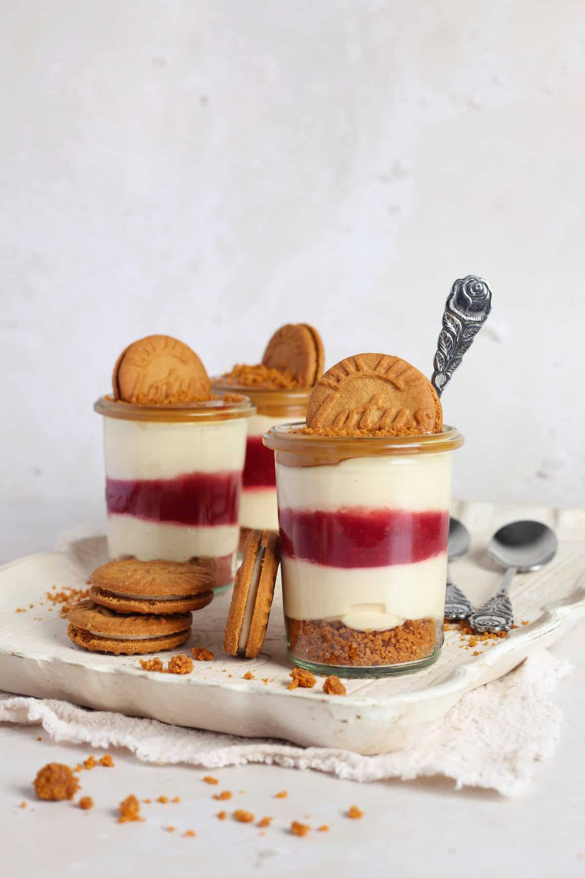 Three glasses of Lotus Biscoff dessert with raspberries on a rustic, light-colored serving tray.