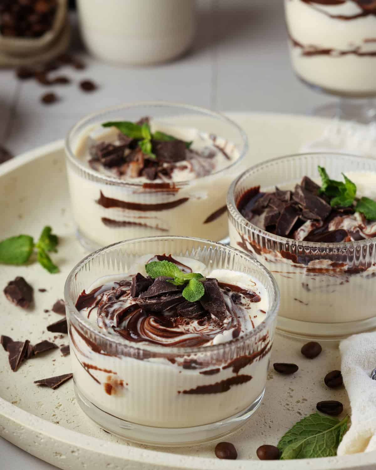 Three round glass bowls of mocha mousse on a round serving tray.