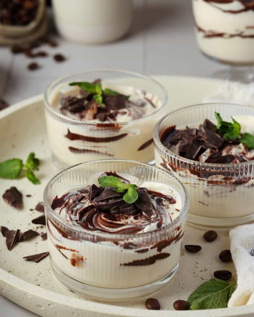 Three round glass bowls with mocha mousse on a round serving tray.