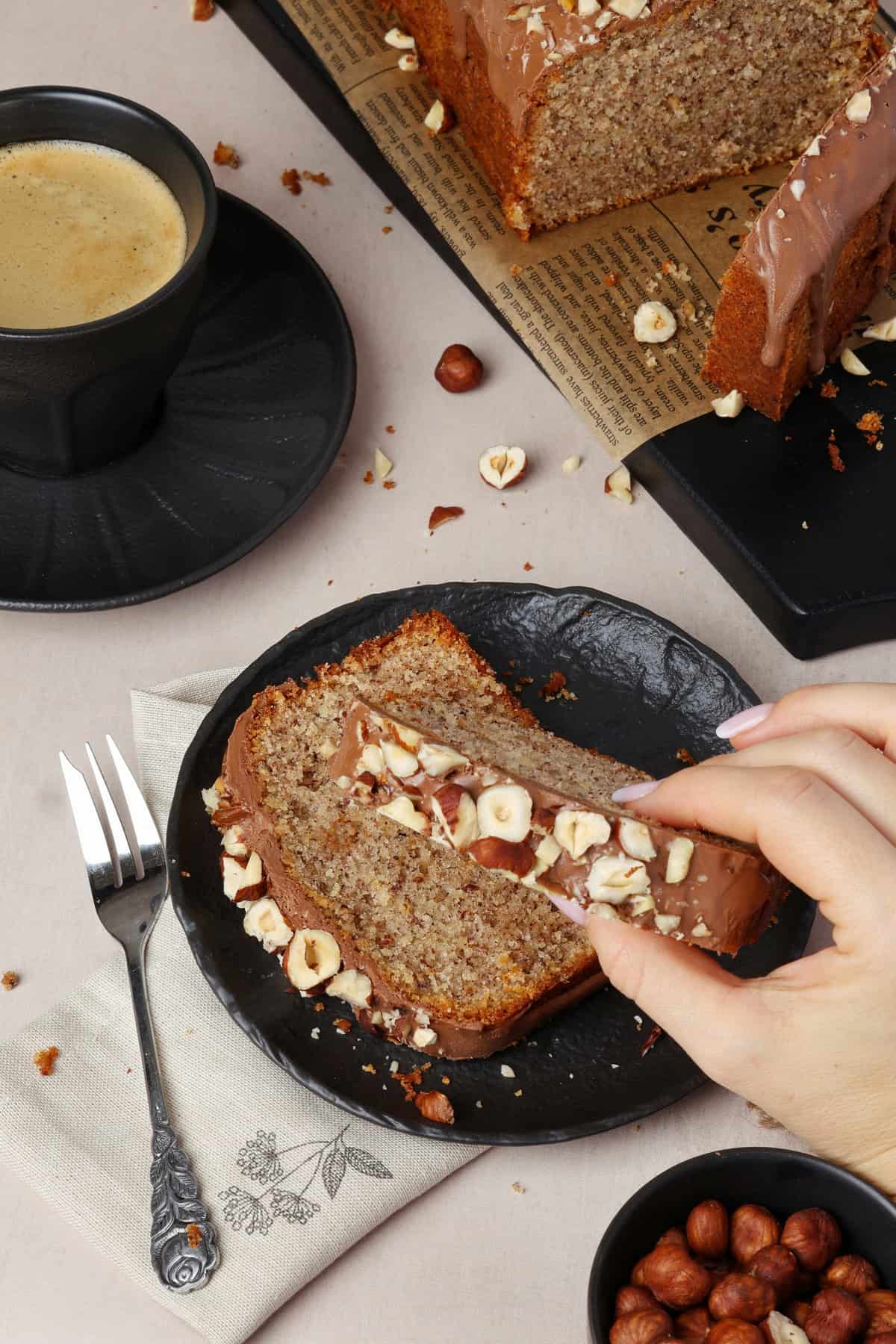 A hand placing a slice of nut cake onto a plate that already has a slice of nut cake on it.